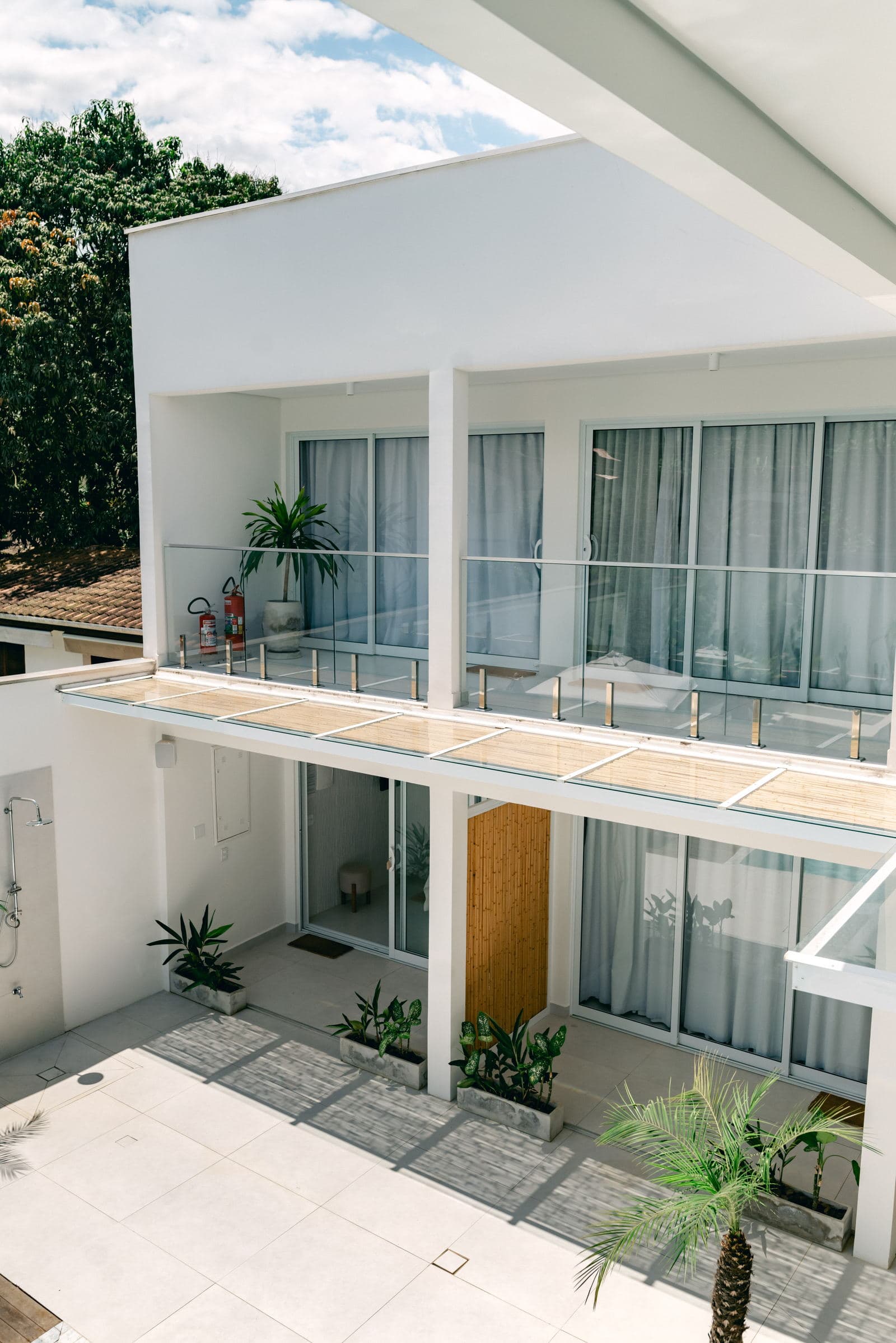 Os dois andares de suítes vistos do pátio, com as cortinas claras nas varandas e o deck de madeira embaixo
