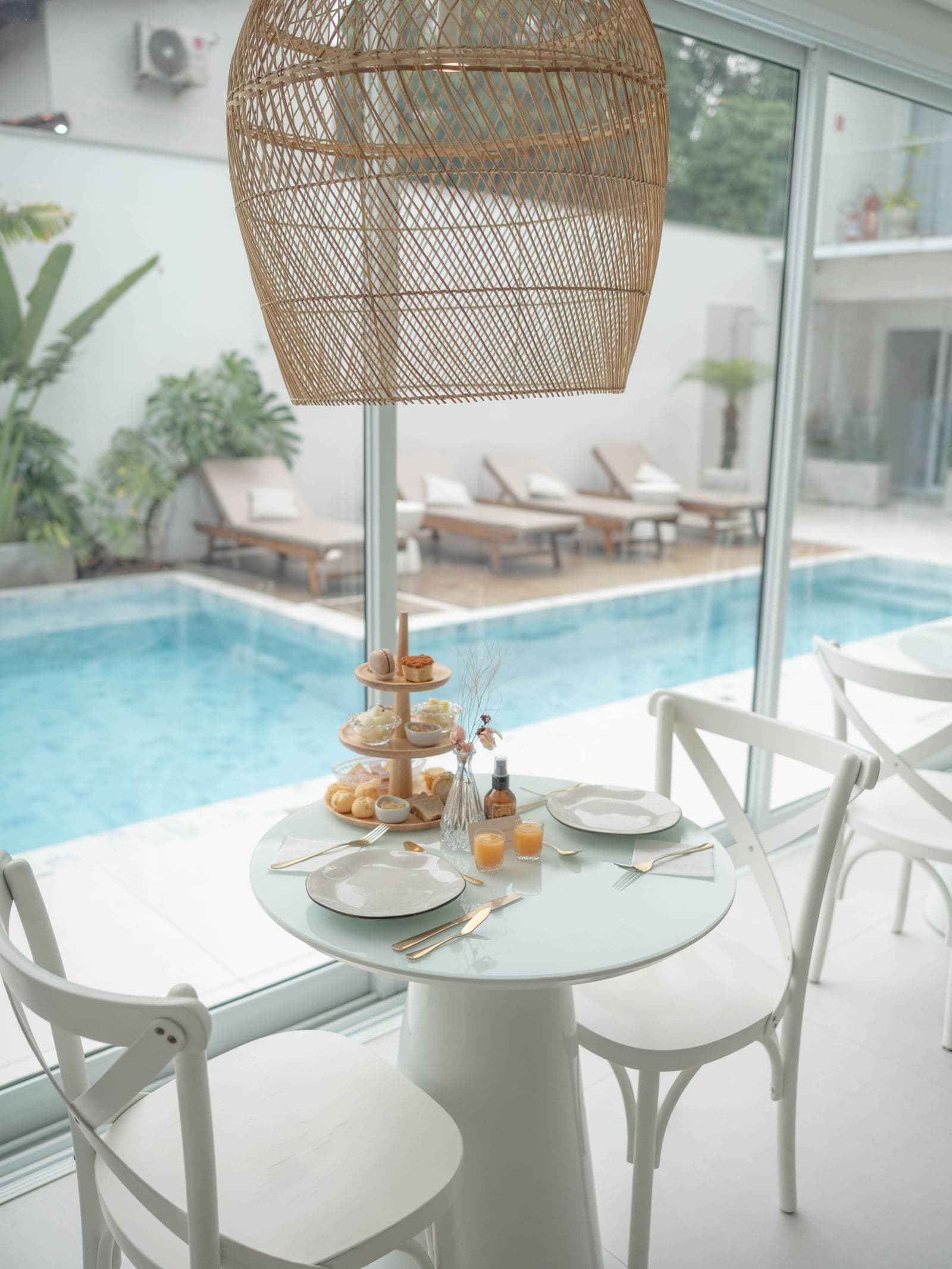 Mesa redonda de café da manhã sob a luminária de palha, com a torre servida e a piscina ao fundo