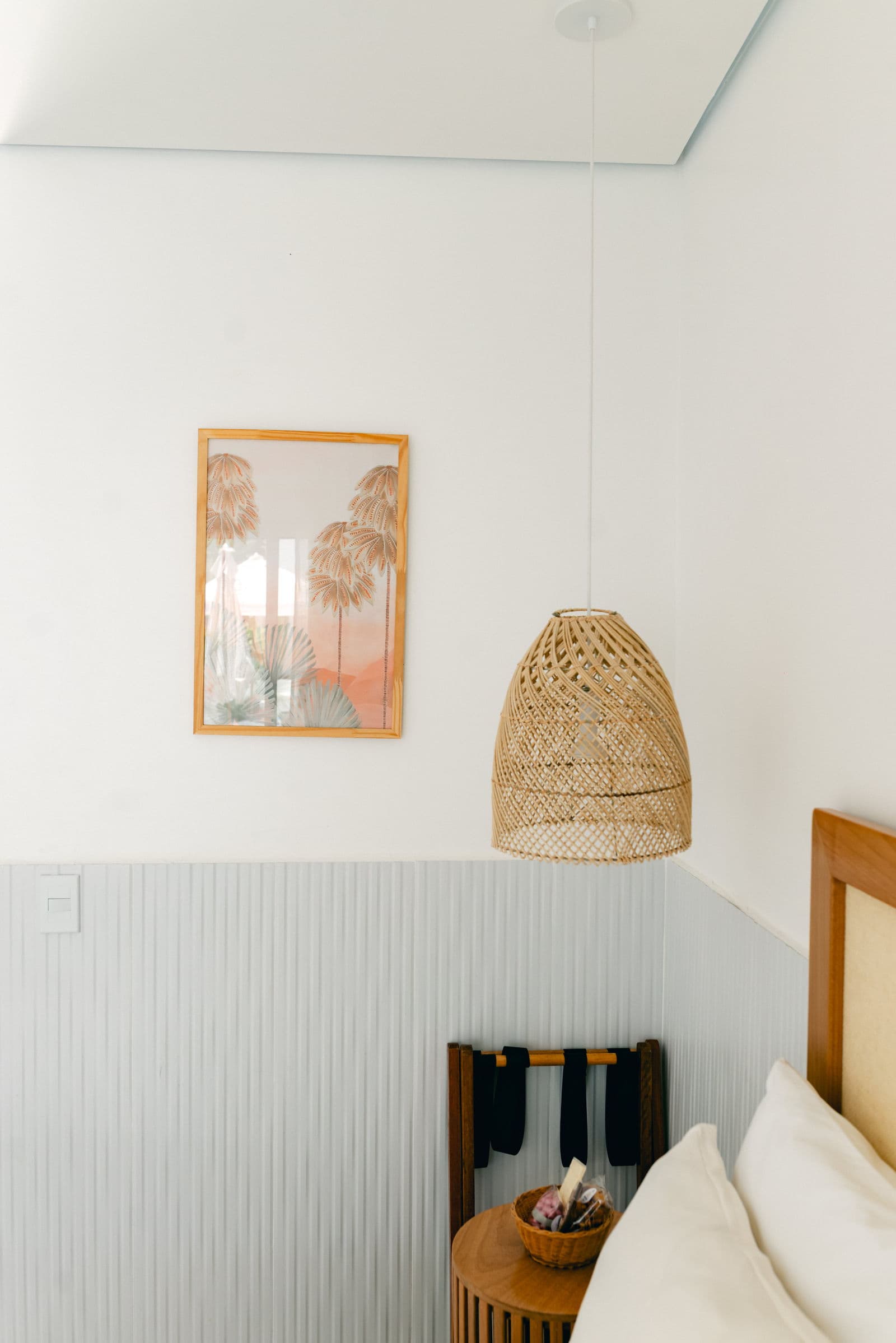 Canto da Suíte Luxo com quadro de palmeiras, luminária de palha e mesa lateral de madeira ripada